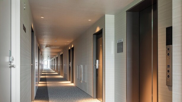 Un pasillo moderno de hotel con un largo recorrido, puertas y un ascensor.