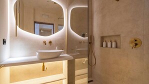 Une salle de bain moderne avec un grand miroir ovale, un lavabo blanc et une douche séparée par une paroi de verre.