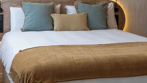 Un lit bien fait, avec une couverture marron, plusieurs coussins de différentes couleurs et une lampe fixée au mur.
