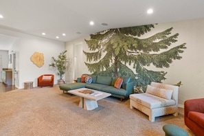 Un salon avec une grande fresque représentant un arbre, un canapé, une table basse et un fauteuil rouge.
