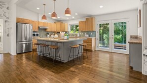 A modern kitchen with a central island, stainless steel appliances, wooden cabinets, and pendant lighting. - 6.5 acres all to yourself! Dog-Friendly Creekside Home w/ Hot Tub, Game Room. 15 minutes to town (White Salmon)