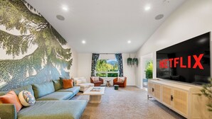 A living room with a sofa, armchairs, a coffee table, a TV, and a mural on the wall. - 6.5 acres all to yourself! Dog-Friendly Creekside Home w/ Hot Tub, Game Room. 15 minutes to town (White Salmon)
