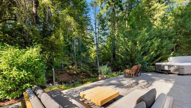 An outdoor seating area with a sofa, chairs, and a table, surrounded by dense greenery and trees. - 6.5 acres all to yourself! Dog-Friendly Creekside Home w/ Hot Tub, Game Room. 15 minutes to town (White Salmon)