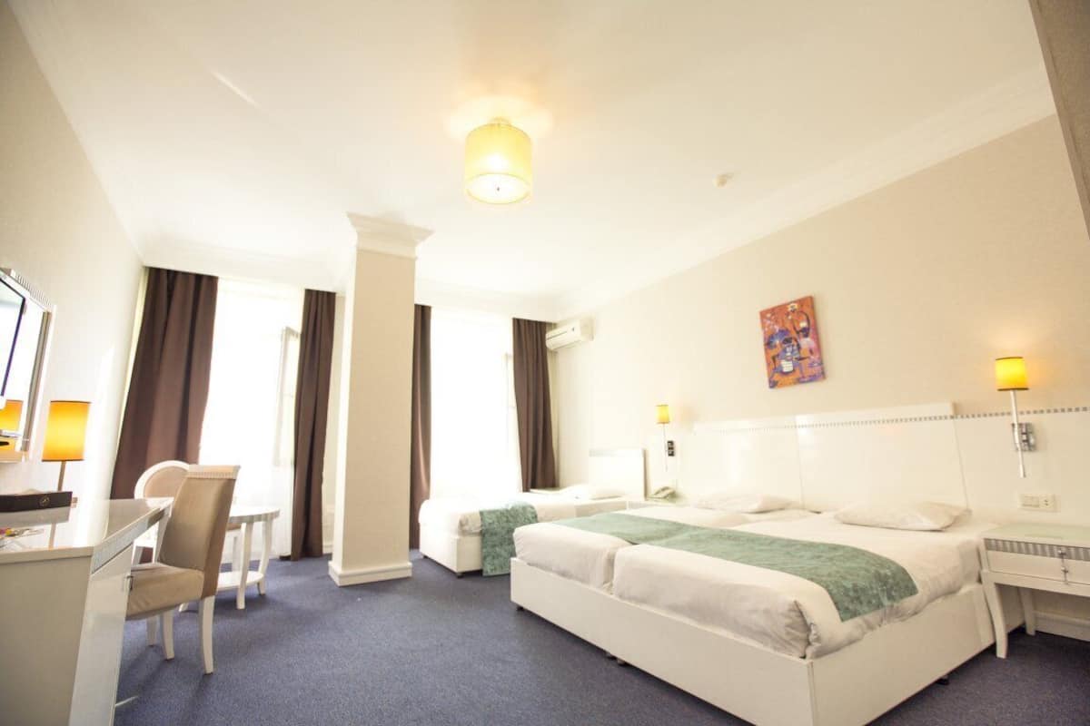 A hotel room with two beds, a desk, a chair, and a painting on the wall.