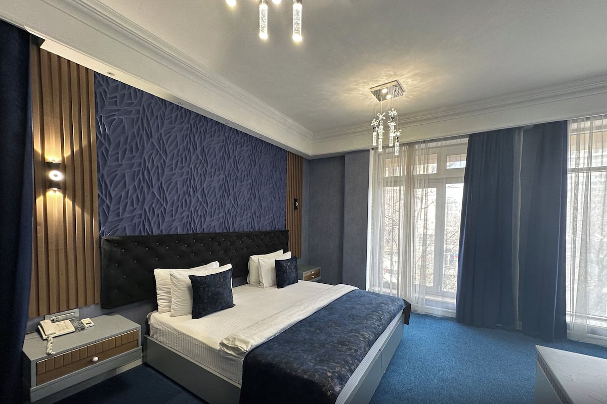 A modern hotel room with a large bed, a nightstand, a telephone, and a window with curtains.