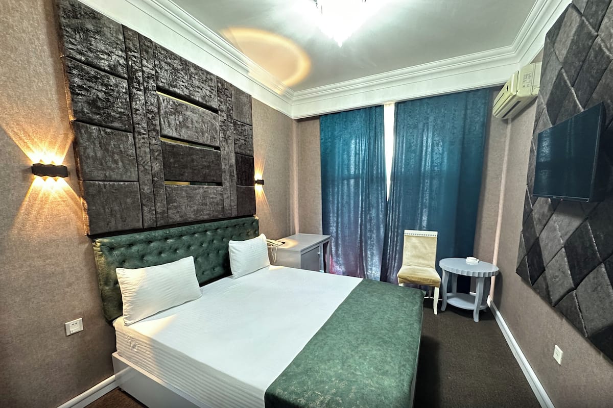 A hotel room with a large bed, a small table, a chair, and a TV mounted on the wall.