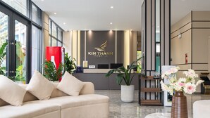 A reception area with a sofa, potted plants, a reception desk, and a vase with flowers.
