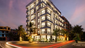A multi-story hotel with balconies, a well-lit entrance, and palm trees.