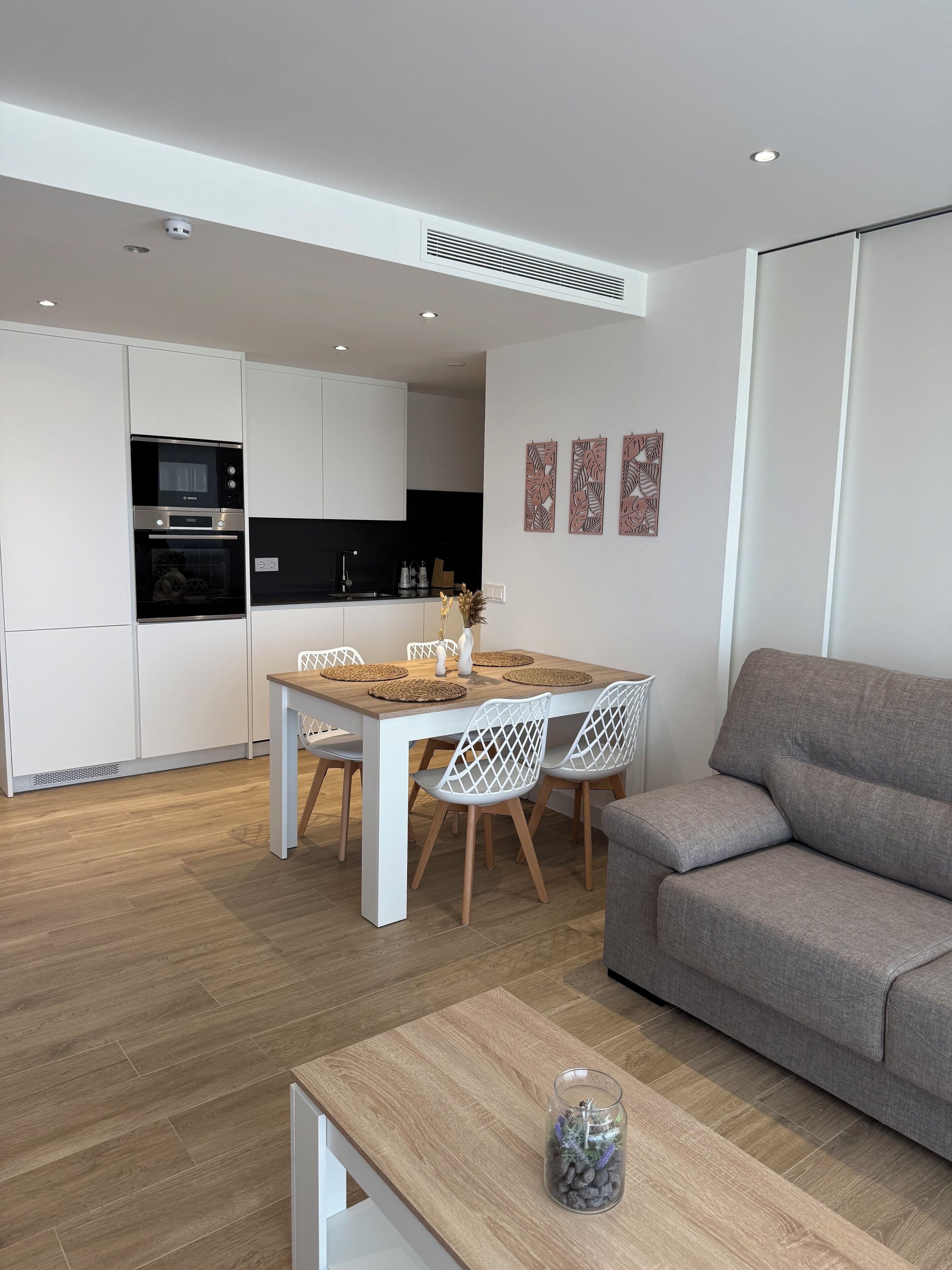 A modern kitchen with white cabinets, a black microwave, and a dining area with a wooden table and white chairs.