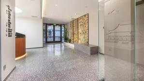 Un moderno vestíbulo de hotel con piso pulido de aspecto moteado, señalización direccional, una mesa de recepción y un separador de vidrio con obras de arte.