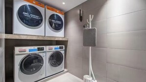 Un área de lavandería con dos lavadoras y una secadora, un perchero de toallas en la pared y un dispensador de papel higiénico.
