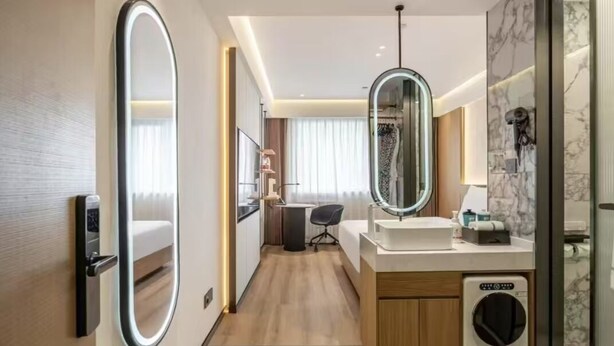 Un baño de hotel moderno con un espejo grande, un lavamanos, una ducha y una lavadora integrada.