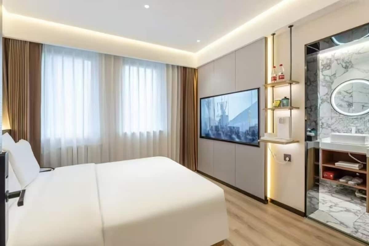 A hotel room with a large bed, a TV mounted on the wall, a bathroom with a marble vanity, and a shelf with toiletries.