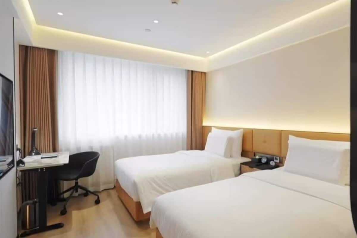 A hotel room with two beds, a desk, a chair, and a large window with curtains.