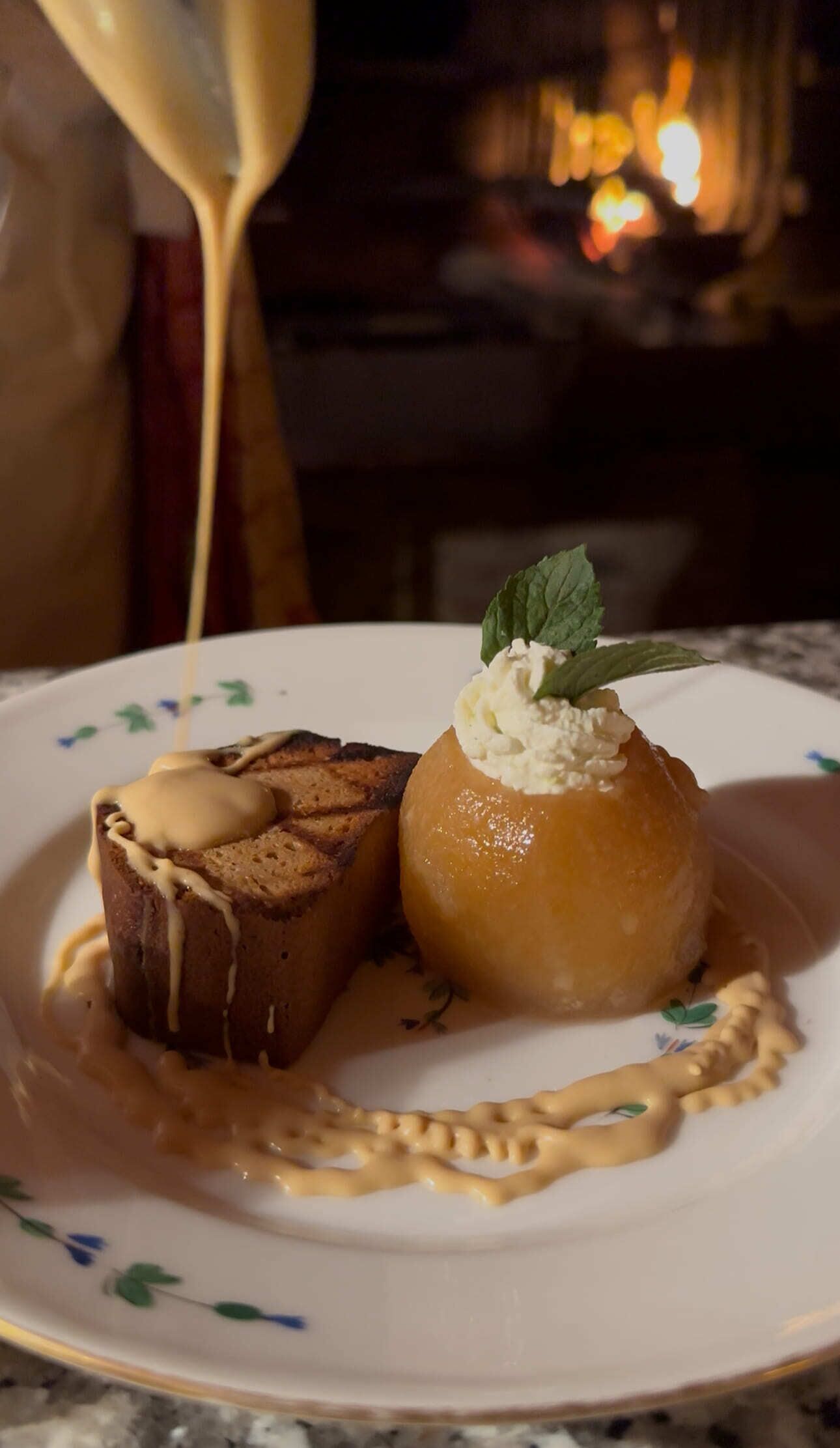 Un plato de postre con un pastel de chocolate y una manzana acaramelada, ambos bañados en salsa cremosa.