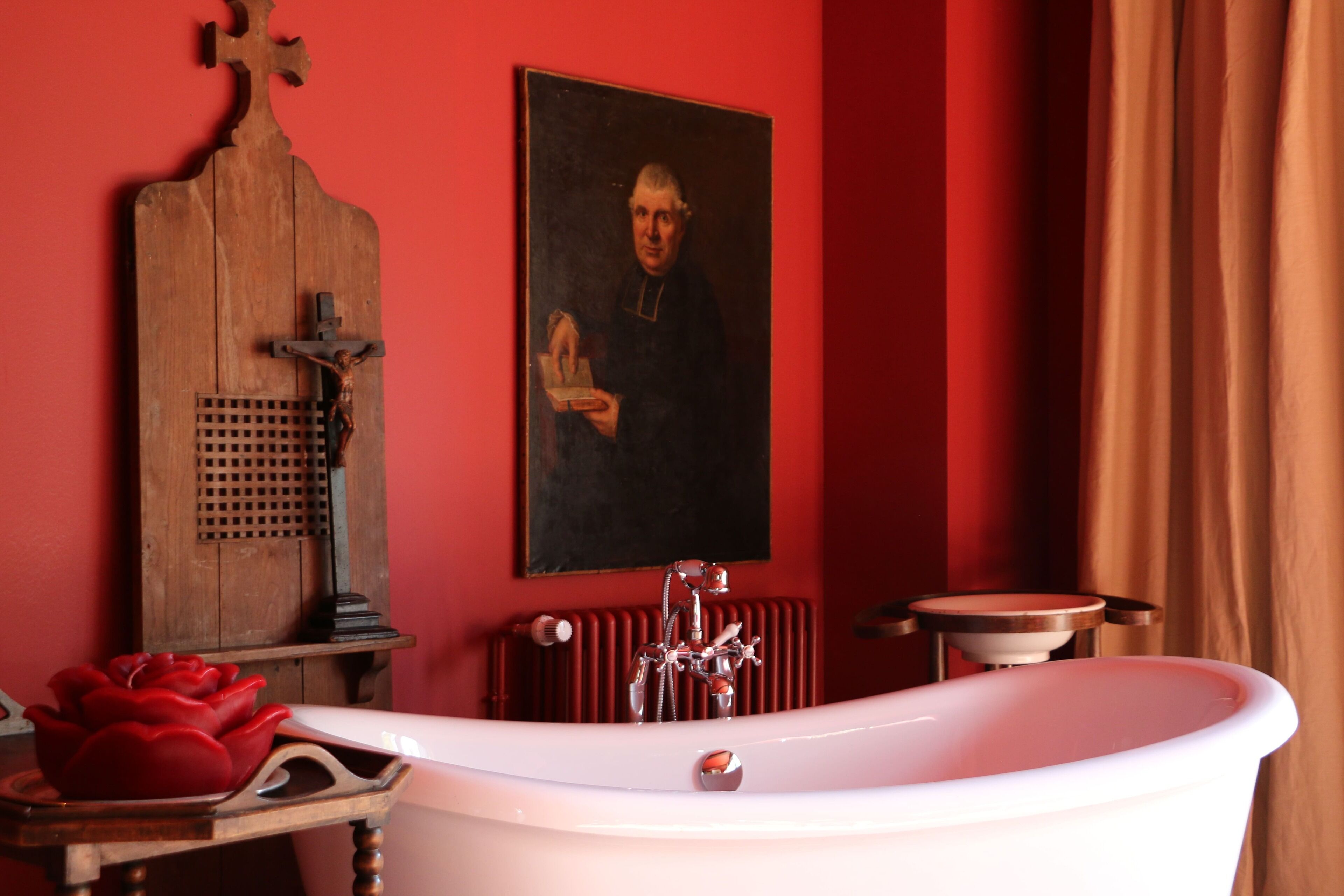 Une salle de bain avec une baignoire blanche, un meuble-lavabo en bois, un mur rouge et un portrait encadré.