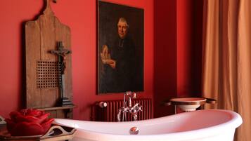Une salle de bain avec une baignoire blanche, un meuble-lavabo en bois, un mur rouge et un portrait encadré.
