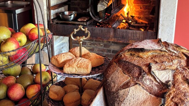 A fireplace with a fire, surrounded by various food items like bread and apples. - Auberge Bout de Bois (Saint-Jouin-Bruneval)