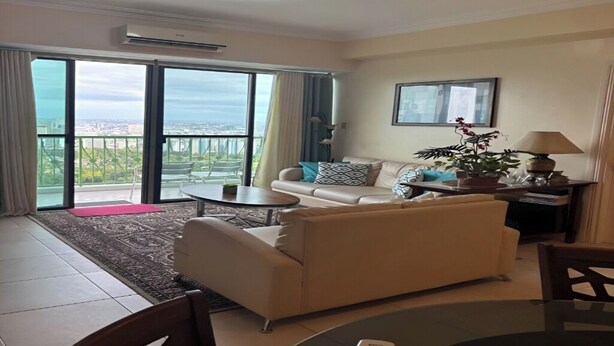 A living room with a sofa, a coffee table, a dining table, and a view through large glass doors to the outside. - CityHouse A (Cebu)