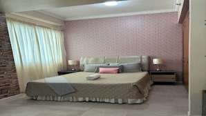 A bedroom with a bed, two bedside tables, a nightstand, a lamp, a curtain, and a wall with a patterned design. - CityHouse A (Cebu)