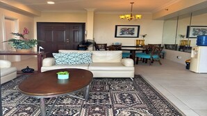 A living room with a sofa, coffee table, patterned rug, dining area with chairs, and a large mirror. - CityHouse A (Cebu)