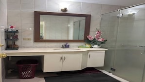 A bathroom with a white sink, mirror, and cabinets, a glass shower enclosure, and a red basket. - CityHouse A (Cebu)