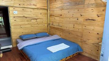 A wooden-paneled room with a bed, a fan, and a door.