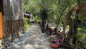 Un sendero conduce a un edificio rústico con cerca de madera y una maceta con flores rosas.