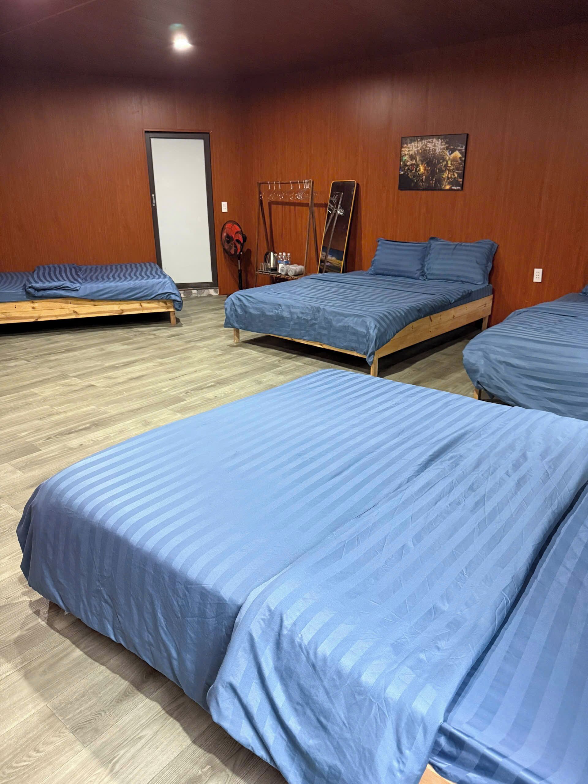 Ein Zimmer mit drei hölzernen Betten, einer Tür, einem Kleiderhaken und einem gerahmten Bild an der Wand.