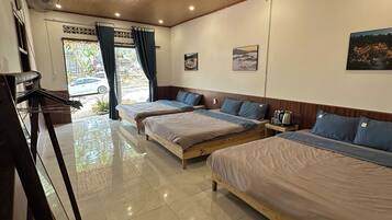 A hotel room with three beds, a fan, a window with curtains, and a picture on the wall.