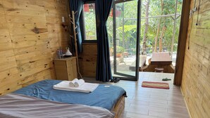 Una habitación de madera con una cama, una mesita de noche y vistas a un espacio exterior a través de una puerta de cristal.