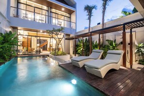 Un edificio moderno de dos pisos con piscina, sillas de descanso y un patio cubierto.