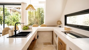 A modern kitchen with a large window, a hanging light fixture, and a view of greenery outside. - Boho Retreat 3BR Enclosed Lounge 5min Beach (Canggu)