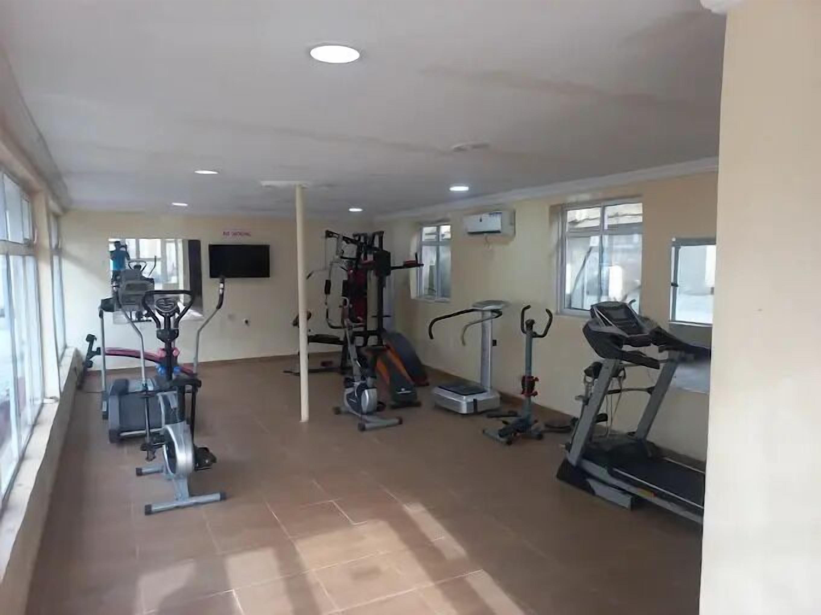 A gym with various exercise equipment, including treadmills and weight machines, and large windows providing natural light.