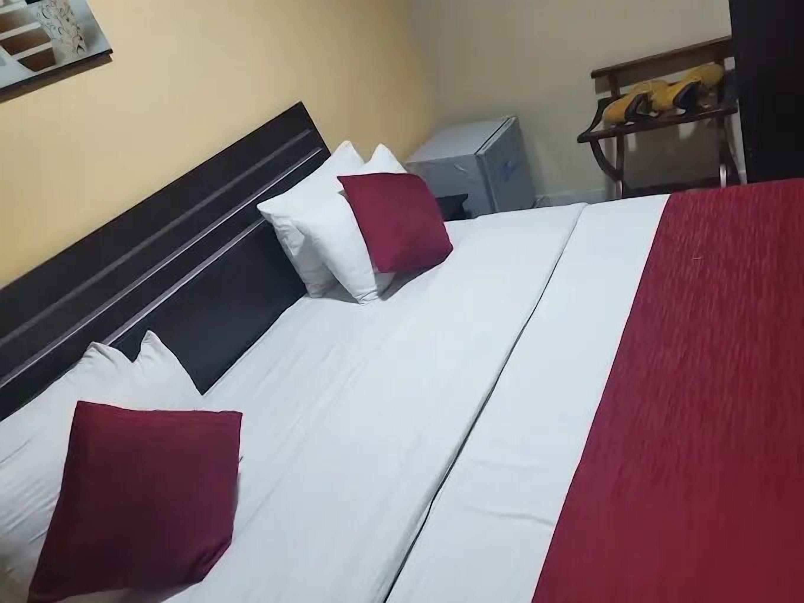 A bed with white bedding and red pillows, a bedside table, and a small desk with a chair.