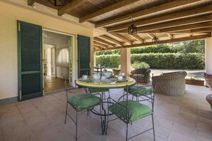 A covered outdoor patio with a round table, green cushioned chairs, and a wicker sofa.