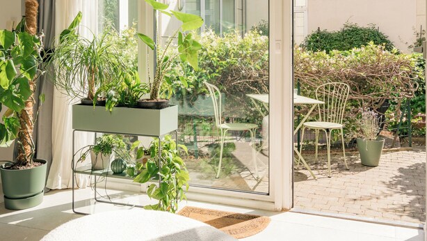 A modern room with a large sliding glass door leading to a garden, a green sofa, and a small table with chairs.