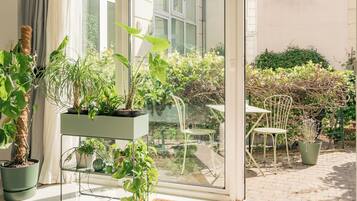 A modern room with a large sliding glass door leading to a garden, a green sofa, and a small table with chairs.