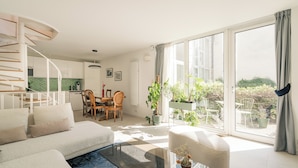 A modern living room with a sofa, a glass coffee table, and a dining area with chairs and a table.