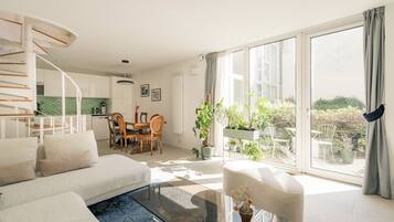A modern living room with a sofa, a glass coffee table, and a dining area with chairs and a table.