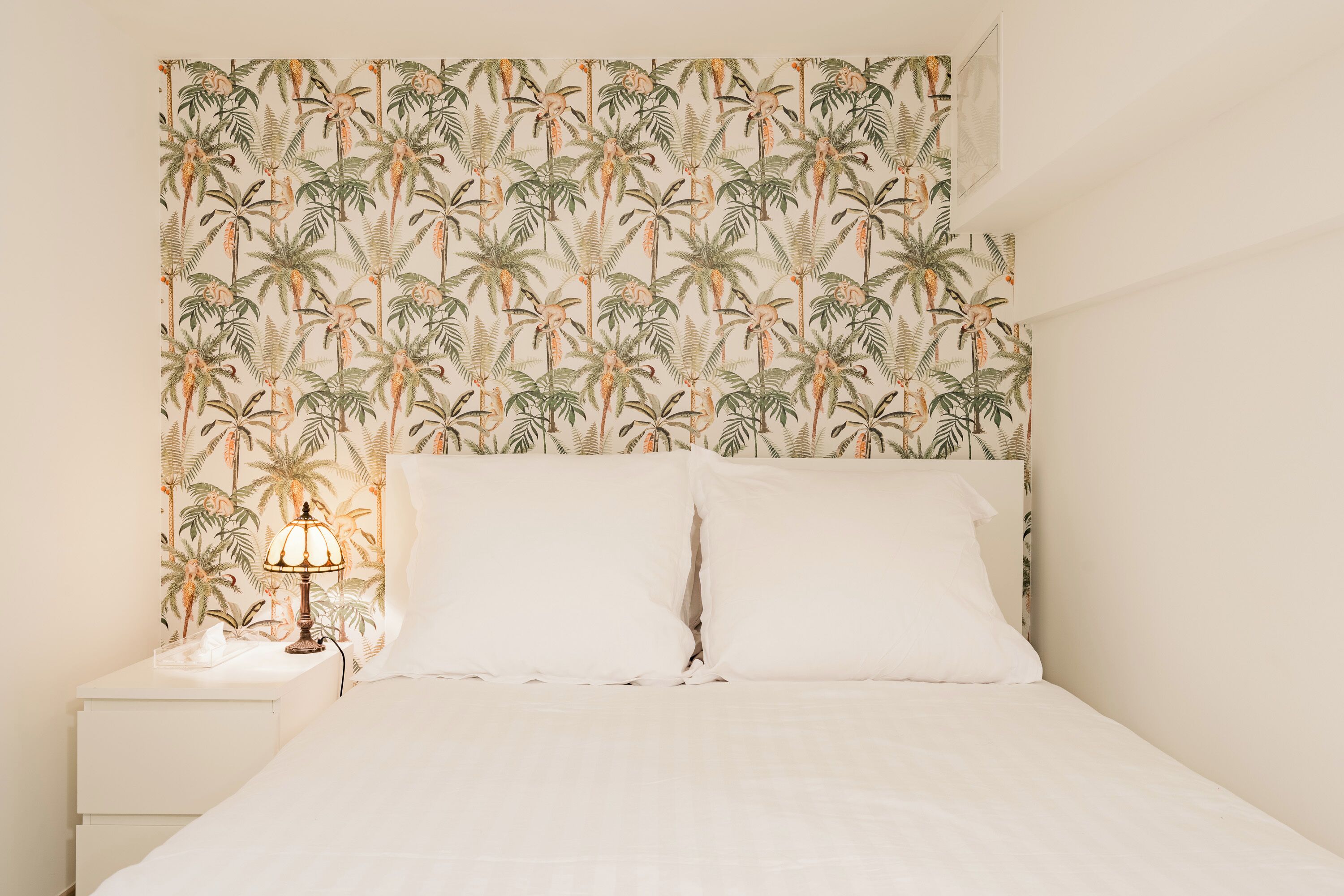 A bed with white linens and a headboard with a tropical leaf pattern.