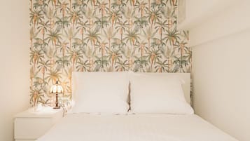 A bed with white linens and a headboard with a tropical leaf pattern.
