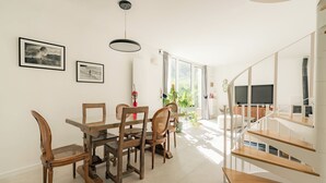 A dining area with a glass table and wooden chairs, a staircase with wooden steps, and a TV in the background.