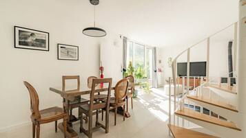 A dining area with a glass table and wooden chairs, a staircase with wooden steps, and a TV in the background.