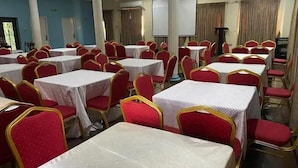 A banquet hall with multiple round tables and red chairs, white tablecloths, and a projector screen. - IBD Hotel and Suites (Abeokuta)