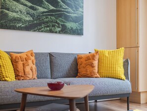 A grey sofa with yellow and orange textured pillows, a small wooden table with a bowl, and a large landscape painting on the wall. - The Shoreditch Warehouse, by Veeve (London)