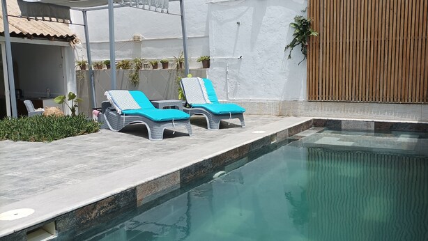 A swimming pool with two lounge chairs and a wooden wall. - Atypical house with swimming pool (Douaouda)