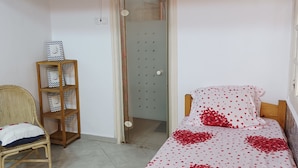 A bedroom with a bed covered in red heart-patterned bedding, a wicker chair with a cushion, and a wooden shelf with decorative items. - Atypical house with swimming pool (Douaouda)
