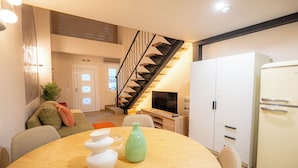 A modern living room with a wooden dining table, a green vase, and a staircase leading to another room. - Vayas Residences Agora (Trikala)