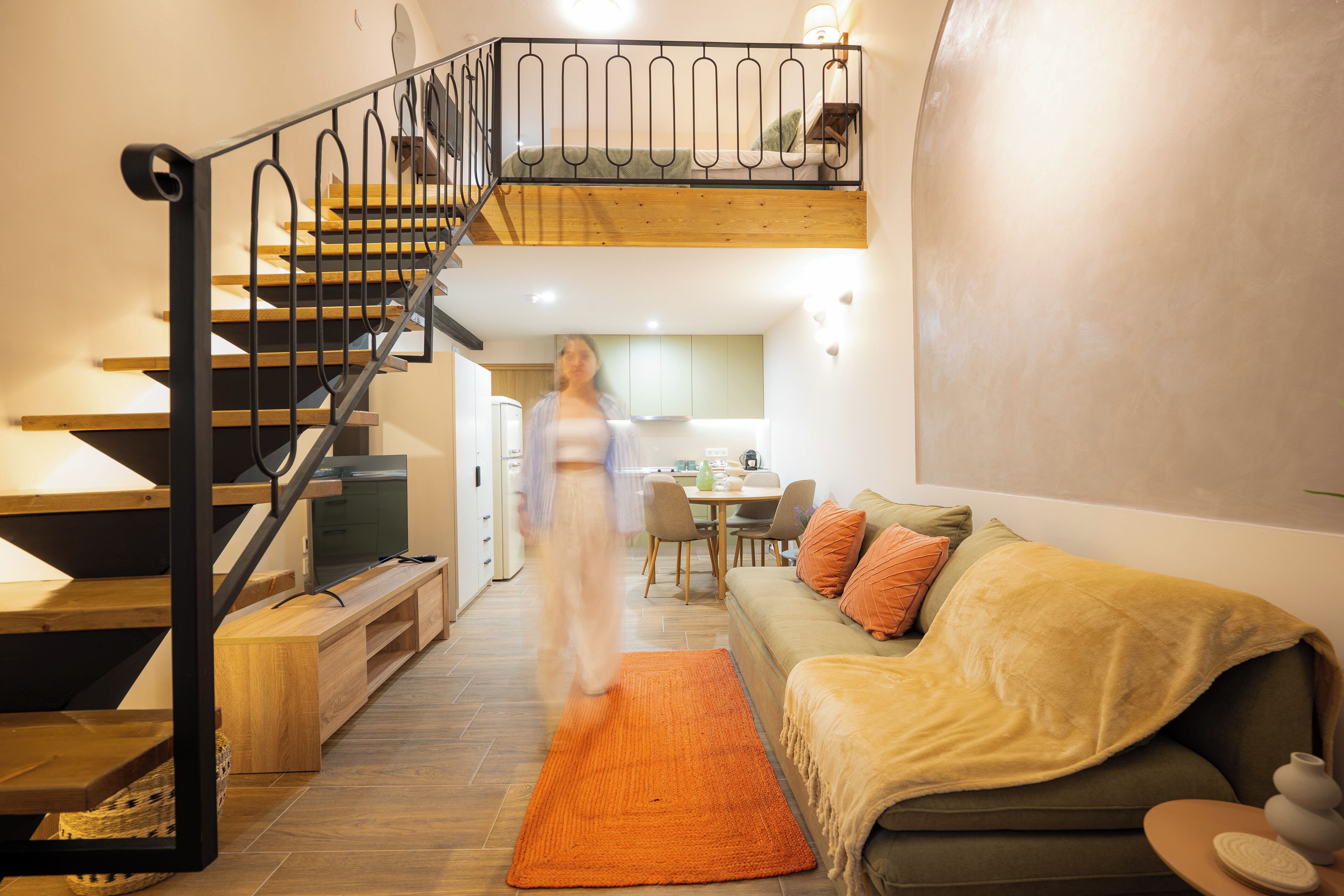A modern interior with a wooden staircase, a sofa, and a dining area.